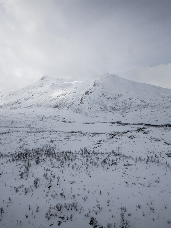 Aerial view of snow covered mountain peaks and a valley with sparse winter vegetation under a cloudy sky Ersfjord Troms Norway. Aerial view of snow covered mountain peaks and a valley with sparse winter vegetation under a cloudy sky Ersfjord Troms Norway.