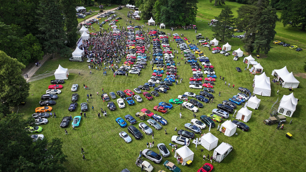 La Chapelle de Guinchay France 01 June 2024 Aerial view of a car show with rows of colorful sports cars on a green lawn with people walking among white tents and lush trees.
