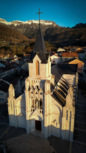 Aerial view of Eglise Saint Pierre with its prominent spire and stone architecture overlooking the town rooftops and snow capped Jura mountains in Gex Auvergne Rhone Alpes France. Aerial view of Eglise Saint Pierre with its prominent spire and stone architecture overlooking the town rooftops and snow capped Jura mountains in Gex Auvergne Rhone Alpes France.