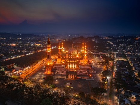 Aerial view of the illuminated Baitul Muttaqien Mosque at the East Kalimantan Islamic Center surrounded by the city lights of Samarinda East Kalimantan Indonesia.