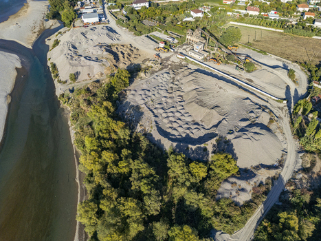 Aerial view of a gravel extraction site with piles of sand and stone heavy machinery and surrounding trees near the Drin River in Bahcallek Shkoder County Albania.