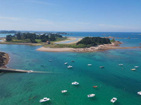 Aerial view of Plage de Port Blanc with small white boats anchored in turquoise water near green islands under a clear blue sky in Penvenan Bretagne France. Aerial view of Plage de Port Blanc with small white boats anchored in turquoise water near green islands under a clear blue sky in Penvenan Bretagne France.