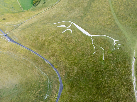 Aerial view of the Uffington White Horse a prehistoric hill figure carved into the chalk hillside surrounded by green rolling hills and a winding road in Faringdon England United Kingdom. Aerial view of the Uffington White Horse a prehistoric hill figure carved into the chalk hillside surrounded by green rolling hills and a winding road in Faringdon England United Kingdom.