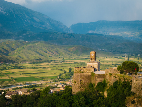 Aerial view of the historic Gjirokaster Fortress with its iconic clock tower overlooking the lush Drino valley and surrounding mountains Gjirokaster Gjirokaster County Albania. Aerial view of the historic Gjirokaster Fortress with its iconic clock tower overlooking the lush Drino valley and surrounding mountains Gjirokaster Gjirokaster County Albania.
