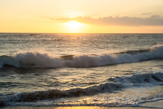 View of ocean waves crashing on the sandy beach under a golden sunset sky Galle Southern Province Sri Lanka.