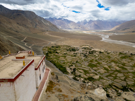 Aerial view of the historic monastery overlooking the vast Zanskar valley with its patchwork of green agricultural fields winding river and rugged mountains in Zanskar Ladakh India.