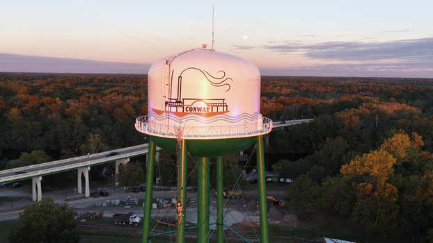 Aerial view of the Conway water tower illuminated by golden hour light surrounded by lush autumn trees and a nearby bridge in Conway South Carolina United States. Aerial view of the Conway water tower illuminated by golden hour light surrounded by lush autumn trees and a nearby bridge in Conway South Carolina United States.