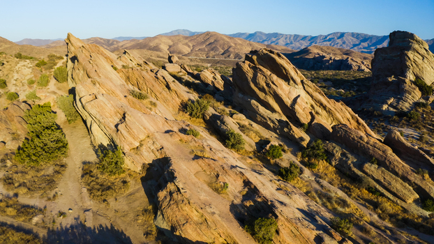 Aerial view of the iconic rock formations at Vasquez Rocks with rugged sandstone cliffs desert shrubs and long shadows under a clear blue sky in the United States. Aerial view of the iconic rock formations at Vasquez Rocks with rugged sandstone cliffs desert shrubs and long shadows under a clear blue sky in the United States.