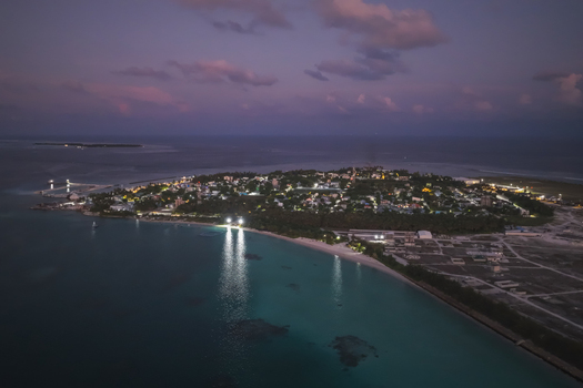 Aerial view of the illuminated island at dusk featuring coastal lights lush palm trees and turquoise waters in Kudahuvadhoo Dhaalu Atoll Maldives. Aerial view of the illuminated island at dusk featuring coastal lights lush palm trees and turquoise waters in Kudahuvadhoo Dhaalu Atoll Maldives.