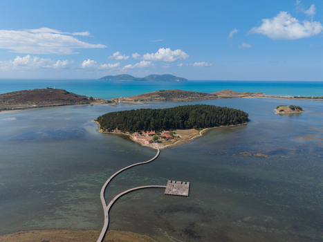 Aerial view of Zvernec Islands featuring the historic monastery lush pine forests and a long wooden footbridge over the shallow lagoon waters in Vlore Vlore County Albania. Aerial view of Zvernec Islands featuring the historic monastery lush pine forests and a long wooden footbridge over the shallow lagoon waters in Vlore Vlore County Albania.