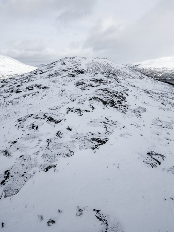 Aerial view of a snow covered mountain ridge with rocky outcrops under a cloudy winter sky in Ersfjord Troms Norway. Aerial view of a snow covered mountain ridge with rocky outcrops under a cloudy winter sky in Ersfjord Troms Norway.