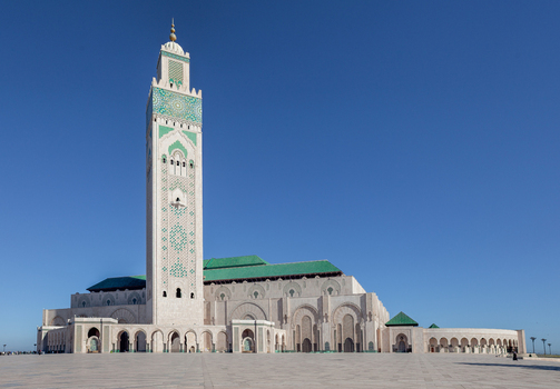 View of the Hassan II Mosque with its iconic tall minaret and intricate green tile work against a clear blue sky in Morocco.