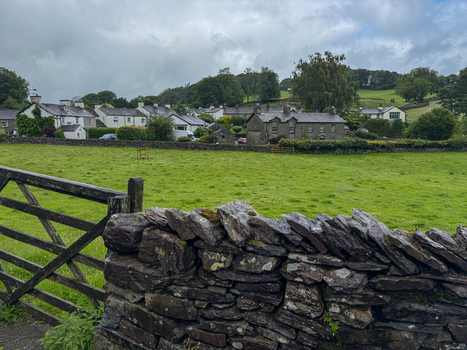 View of traditional stone cottages in the Yorkshire Dales behind a dry stone wall and wooden gate in Hawes England United Kingdom. View of traditional stone cottages in the Yorkshire Dales behind a dry stone wall and wooden gate in Hawes England United Kingdom.