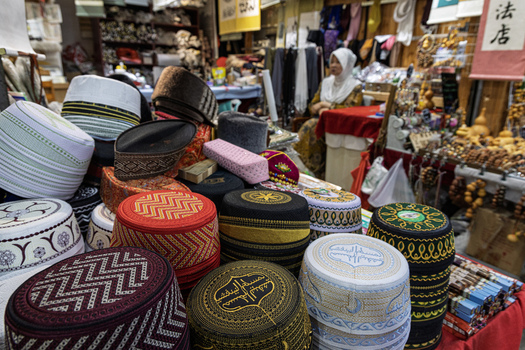Xi an Shaanxi China 14 September 2026 View of traditional embroidered Muslim caps at a market stall with a woman sitting in the background surrounded by wooden crafts.