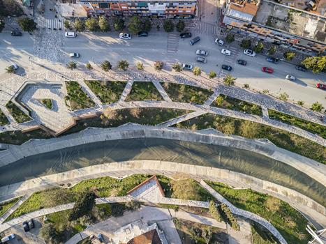 Aerial view of the Gjanica River flowing through the urban landscape with paved walkways green spaces and nearby city streets in Fier Fier County Albania. Aerial view of the Gjanica River flowing through the urban landscape with paved walkways green spaces and nearby city streets in Fier Fier County Albania.