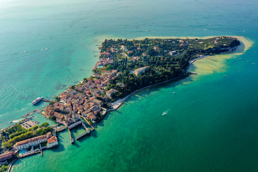 Aerial view of the Scaligero Castle and Villa Cortine on the historic peninsula surrounded by the turquoise waters of Lake Garda in Sirmione Lombardia Italy. Aerial view of the Scaligero Castle and Villa Cortine on the historic peninsula surrounded by the turquoise waters of Lake Garda in Sirmione Lombardia Italy.