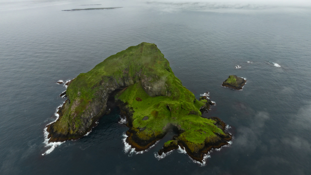 Aerial view of a lush green island surrounded by dark ocean waters and rocky cliffs in Iceland. Aerial view of a lush green island surrounded by dark ocean waters and rocky cliffs in Iceland.