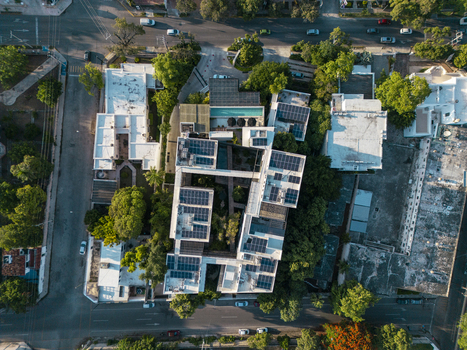Aerial view of a modern building complex featuring solar panels on rooftops lush green trees and a swimming pool in the courtyard in Merida Yucatan Mexico. Aerial view of a modern building complex featuring solar panels on rooftops lush green trees and a swimming pool in the courtyard in Merida Yucatan Mexico.