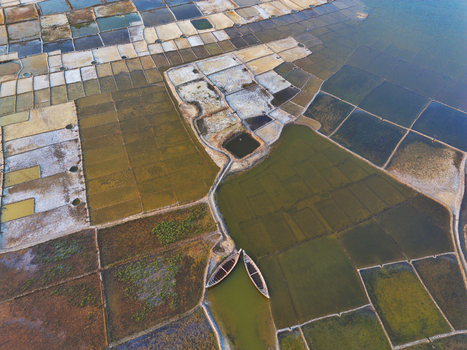 Aerial view of geometric salt pans and evaporation ponds with two wooden boats moored in a narrow channel in Moheskhali Upazila Chittagong Division Bangladesh. Aerial view of geometric salt pans and evaporation ponds with two wooden boats moored in a narrow channel in Moheskhali Upazila Chittagong Division Bangladesh.