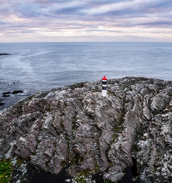 Aerial view of Hamningberg Lighthouse standing on rugged rocky cliffs overlooking the Barents Sea in Hamningberg Finnmark Norway. Aerial view of Hamningberg Lighthouse standing on rugged rocky cliffs overlooking the Barents Sea in Hamningberg Finnmark Norway.