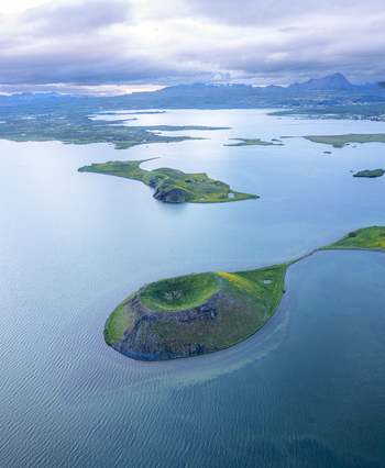 Aerial view of Lake Myvatn featuring volcanic craters surrounded by blue water and green landscapes in Thingeyjarsveit Iceland.