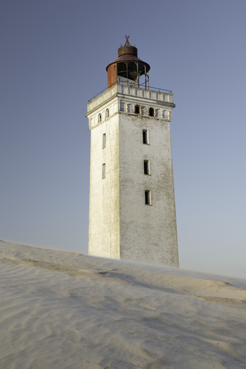 View of the historic Rubjerg Knude lighthouse standing amidst shifting sand dunes under a clear blue sky in Lokken Denmark. View of the historic Rubjerg Knude lighthouse standing amidst shifting sand dunes under a clear blue sky in Lokken Denmark.