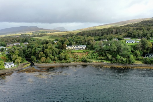 Aerial view of Portree Harbour with its historic buildings nestled along the lush green coastline surrounded by rolling hills and the calm waters of the bay in Portree Scotland United Kingdom.
