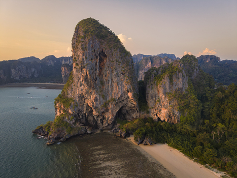 Aerial view of dramatic limestone cliffs rising majestically from turquoise waters fringed by verdant trees and sandy beaches Railay Beach Thailand.