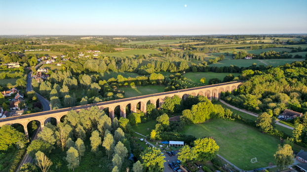 Aerial view of the historic Chappel Viaduct a long brick railway bridge with multiple arches surrounded by lush green trees fields and rural landscape in Chappel England United Kingdom.