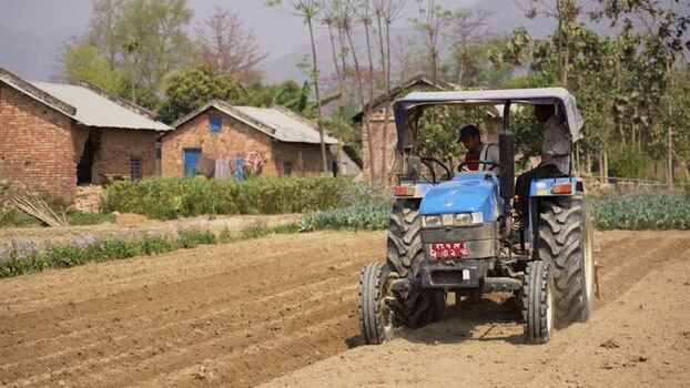 View of a blue tractor plowing a field in Dhangadhi Nepal. View of a blue tractor plowing a field in Dhangadhi Nepal.