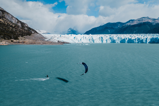 Aerial view of a kitesurfer gliding across the turquoise waters of Lake Argentino in front of the Perito Moreno Glacier with snowy mountains in Perito Moreno Santa Cruz Province Argentina.