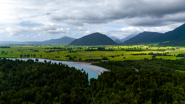 Aerial view of a turquoise river snaking through a verdant valley flanked by dark forests and majestic mountains beneath a cloudy sky Hokitika Gorge West Coast Region New Zealand. Aerial view of a turquoise river snaking through a verdant valley flanked by dark forests and majestic mountains beneath a cloudy sky Hokitika Gorge West Coast Region New Zealand.