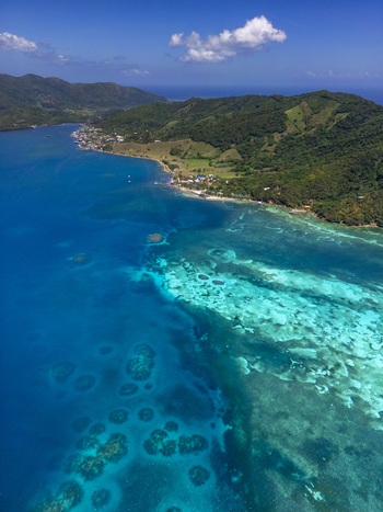 Aerial view of the lush tropical coastline and vibrant turquoise coral reefs under a clear blue sky in Guanaja Bay Islands Department Honduras. Aerial view of the lush tropical coastline and vibrant turquoise coral reefs under a clear blue sky in Guanaja Bay Islands Department Honduras.