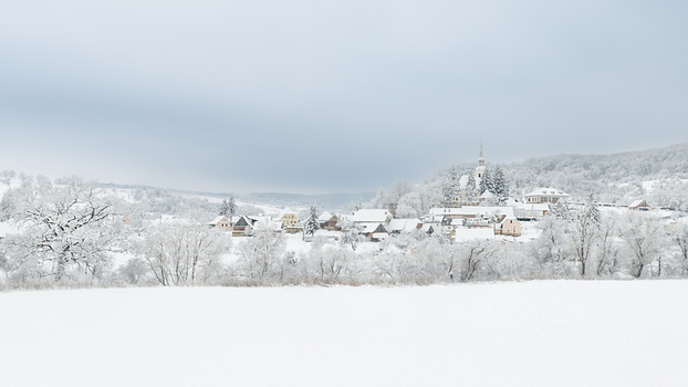 View of the snow covered village of Pestera with its church spire rising above frost laden trees and traditional houses under an overcast winter sky in Pestera Brasov Romania. View of the snow covered village of Pestera with its church spire rising above frost laden trees and traditional houses under an overcast winter sky in Pestera Brasov Romania.