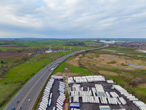 Aerial view of Doxey Marshes with a busy motorway a large logistics yard filled with white semi trailers and wind turbines in the distance in Stafford England United Kingdom. Aerial view of Doxey Marshes with a busy motorway a large logistics yard filled with white semi trailers and wind turbines in the distance in Stafford England United Kingdom.