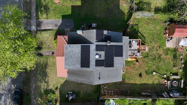 Aerial view of a residential house featuring modern solar panels on the roof surrounded by a green lawn mature trees and a backyard deck in Lynchburg Virginia United States.