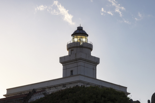 View of the historic Capo Testa lighthouse with its glowing lantern room against a clear blue sky and soft clouds in Capo Testa Sardegna Italy. View of the historic Capo Testa lighthouse with its glowing lantern room against a clear blue sky and soft clouds in Capo Testa Sardegna Italy.