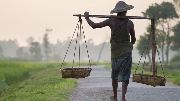 View of a farmer carrying baskets on a rural road Bangladesh.
