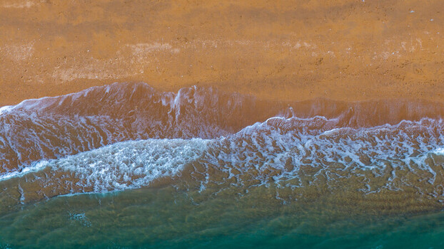 Aerial view of the shoreline with gentle waves washing over the golden sand and turquoise water in West Bay England United Kingdom. Aerial view of the shoreline with gentle waves washing over the golden sand and turquoise water in West Bay England United Kingdom.