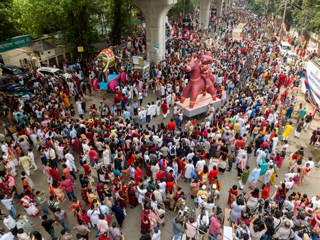 Dhaka Bangladesh 13 April 2026 Aerial view of a vibrant crowd celebrating a festival with large colorful effigies under the grey concrete of an elevated structure.