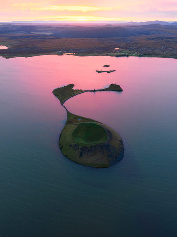 Aerial view of a serene lake reflecting the pink streaked sky with a small island in its center creating a peaceful yet striking scene Myvatn Þingeyjarsveit Iceland. Aerial view of a serene lake reflecting the pink streaked sky with a small island in its center creating a peaceful yet striking scene Myvatn Þingeyjarsveit Iceland.