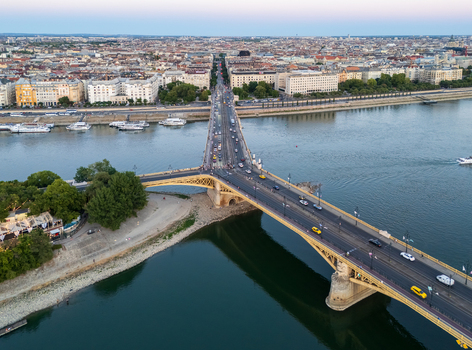 Aerial view of Margaret Bridge carrying traffic and trams across the Danube linking Buda Pest and Margaret Island amid Budapest s riverside cityscape at dusk. Aerial view of Margaret Bridge carrying traffic and trams across the Danube linking Buda Pest and Margaret Island amid Budapest s riverside cityscape at dusk.