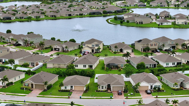 Aerial view of a residential neighborhood with suburban houses manicured lawns and a central lake with a fountain in Cape Coral Florida United States. Aerial view of a residential neighborhood with suburban houses manicured lawns and a central lake with a fountain in Cape Coral Florida United States.