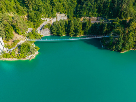 Aerial view of the suspension bridge spanning the turquoise waters of Lac de la Gruyere surrounded by lush green forests and rocky cliffs in Pont la Ville Fribourg Switzerland.