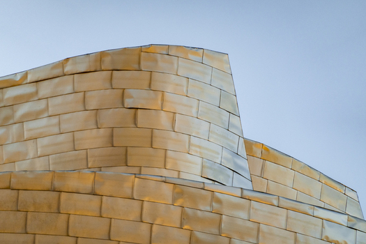 View of the curved titanium panels of the Guggenheim Museum Bilbao reflecting golden light against a clear sky in Bilbao Euskadi Spain. View of the curved titanium panels of the Guggenheim Museum Bilbao reflecting golden light against a clear sky in Bilbao Euskadi Spain.