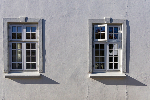 View of two white framed windows on a textured facade with sharp shadows in Ribe Denmark. View of two white framed windows on a textured facade with sharp shadows in Ribe Denmark.