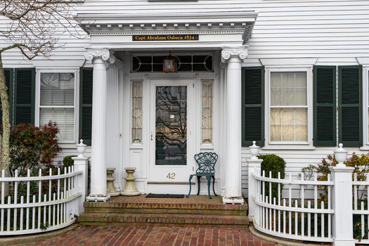 View of the historic Capt Abraham Osborn house entrance featuring white ionic columns green shutters and a white picket fence in Edgartown Massachusetts United States.