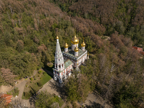 Aerial view of the Shipka Memorial Church with its distinctive golden domes and ornate bell tower nestled among the dense autumn forest in Shipka Stara Zagora Bulgaria. Aerial view of the Shipka Memorial Church with its distinctive golden domes and ornate bell tower nestled among the dense autumn forest in Shipka Stara Zagora Bulgaria.