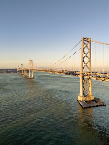 Aerial view of the San Francisco Oakland Bay Bridge spanning the calm waters of the bay during the golden hour with clear skies. San Francisco California United States. Aerial view of the San Francisco Oakland Bay Bridge spanning the calm waters of the bay during the golden hour with clear skies. San Francisco California United States.