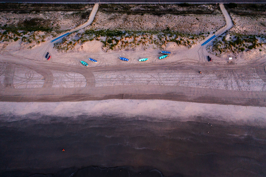 Aerial view of Sea Isle City Beach with small colorful boats resting on the sand tire tracks across the beach and dunes in Sea Isle City New Jersey United States.